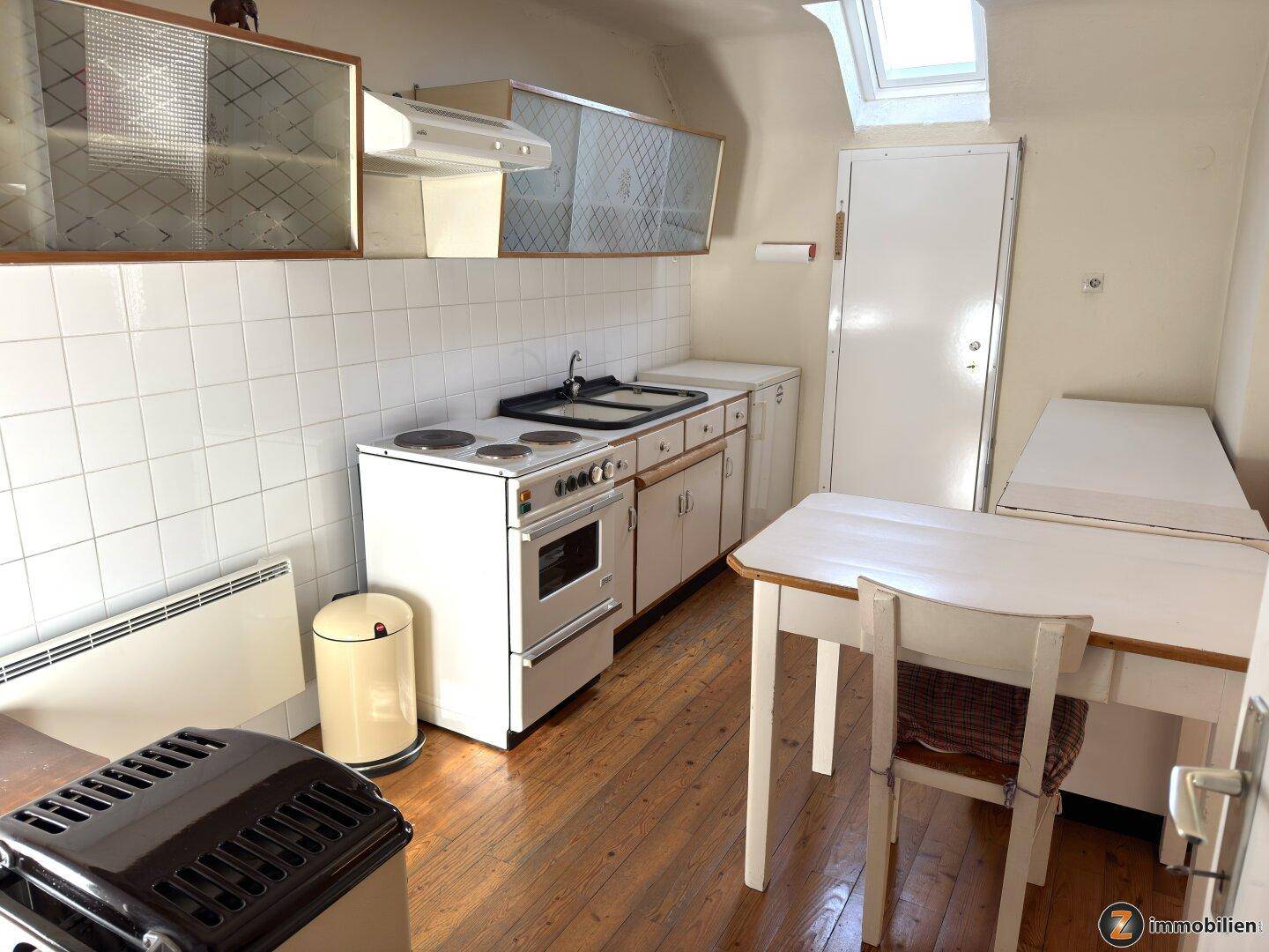 Einfache Küche mit Herd, Spüle und Holzboden, sowie einem Dachfenster für natürliches Licht.
