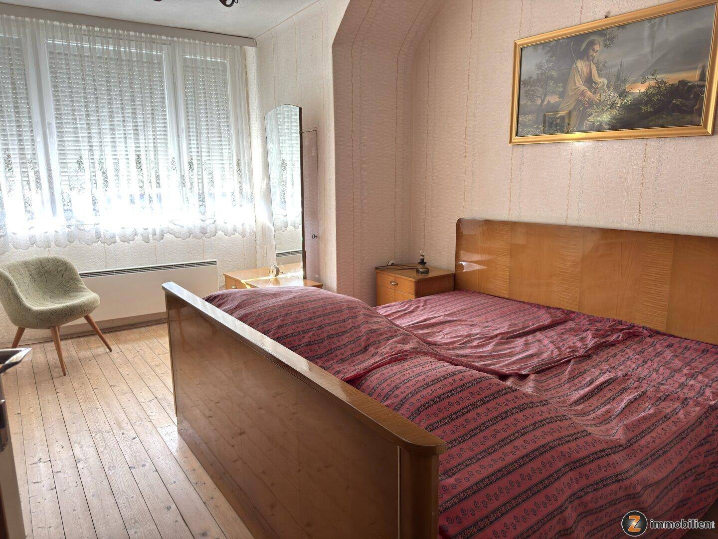 Schlafzimmer mit Doppelbett, Holzboden und großem Fenster, das viel Licht hereinlässt.