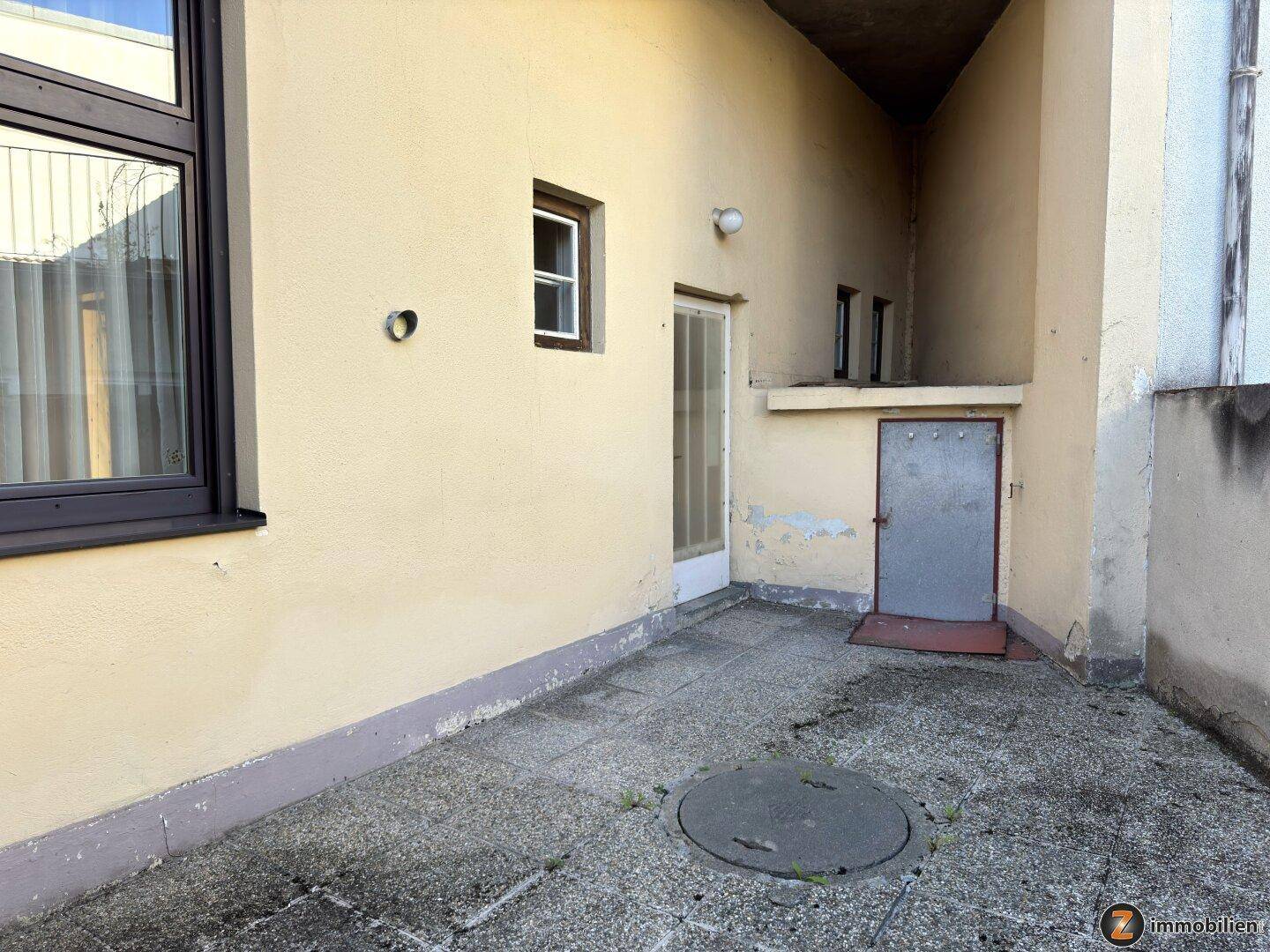 Kleine gepflasterte Terrasse im Freien mit Zugang zu einem Abstellraum, ideal für Entspannung.