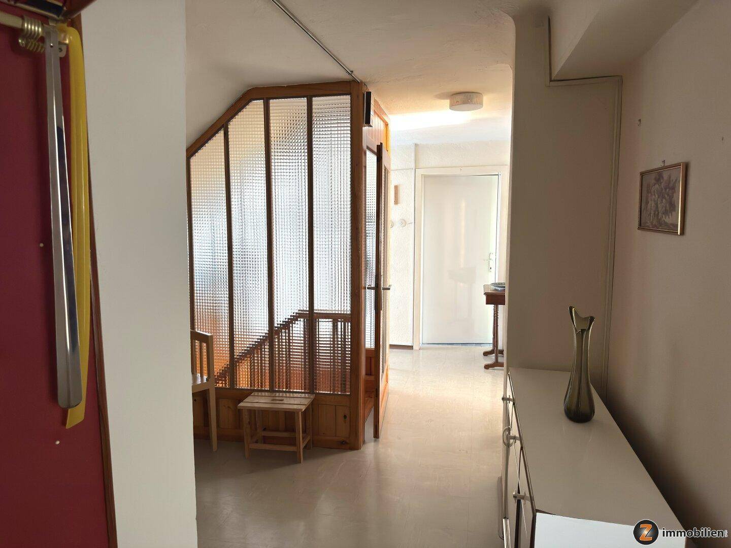 Eingangsbereich mit Holztreppe und Glasabtrennung, die zu den oberen Etagen führt.