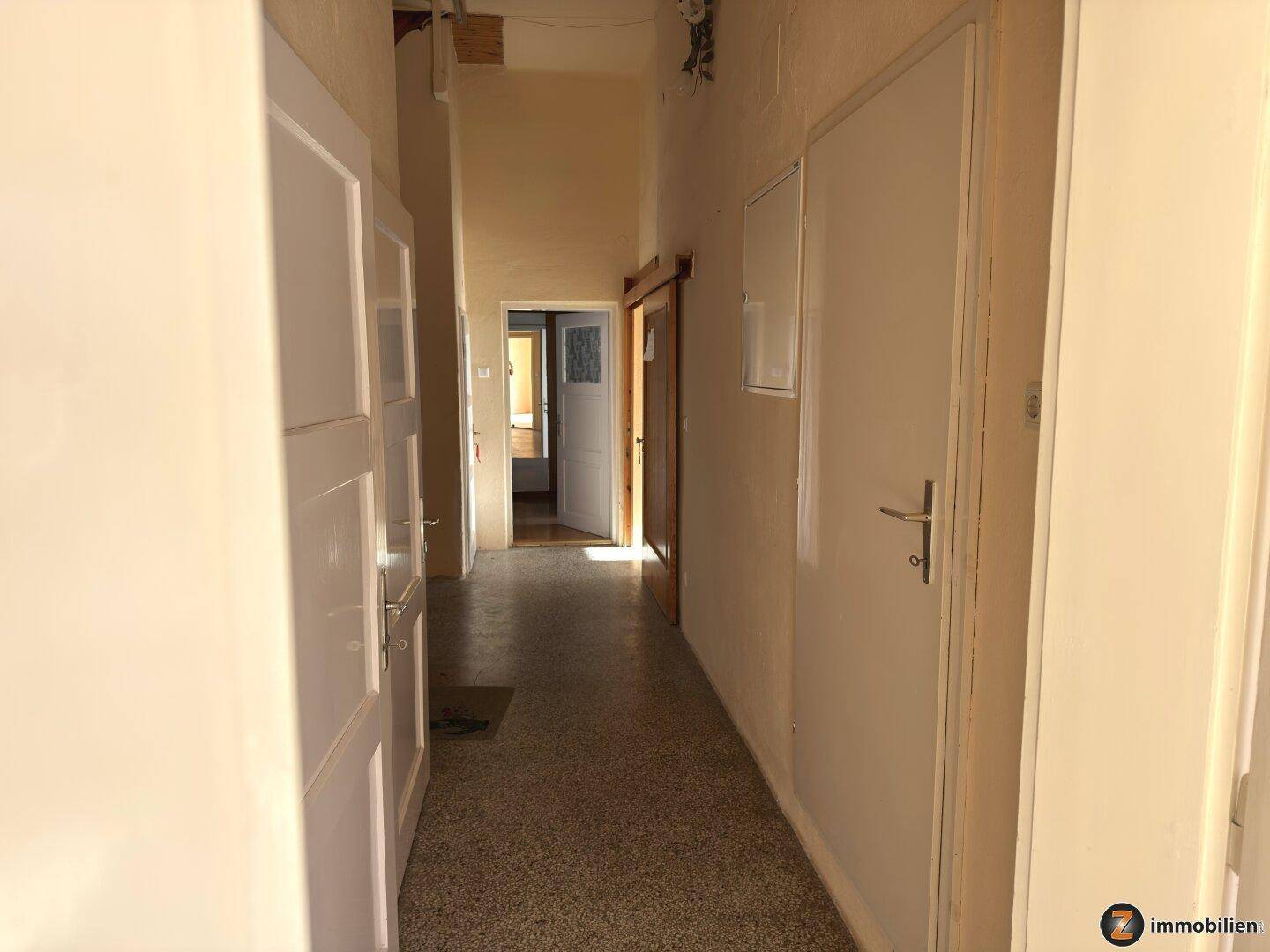 Langer Flur mit mehreren Türen und Terrazzoboden, der zu verschiedenen Bereichen der Wohnung führt.