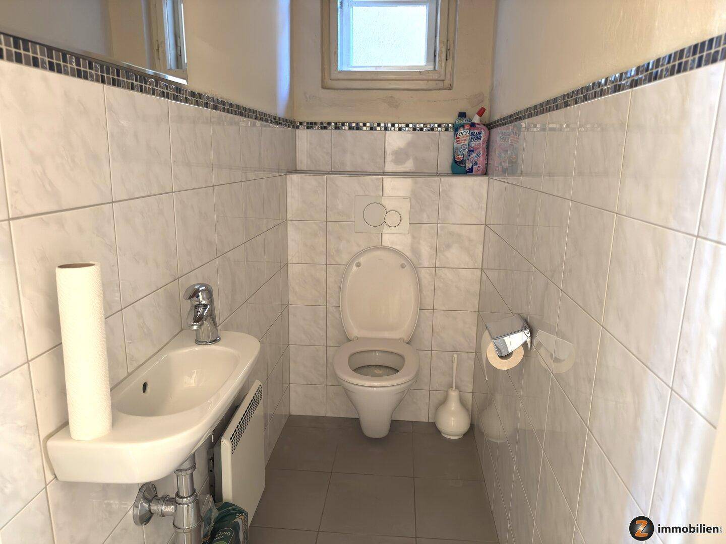 Kleines Gäste-WC mit Fliesen, wandmontierter Toilette und einem kleinen Waschbecken.