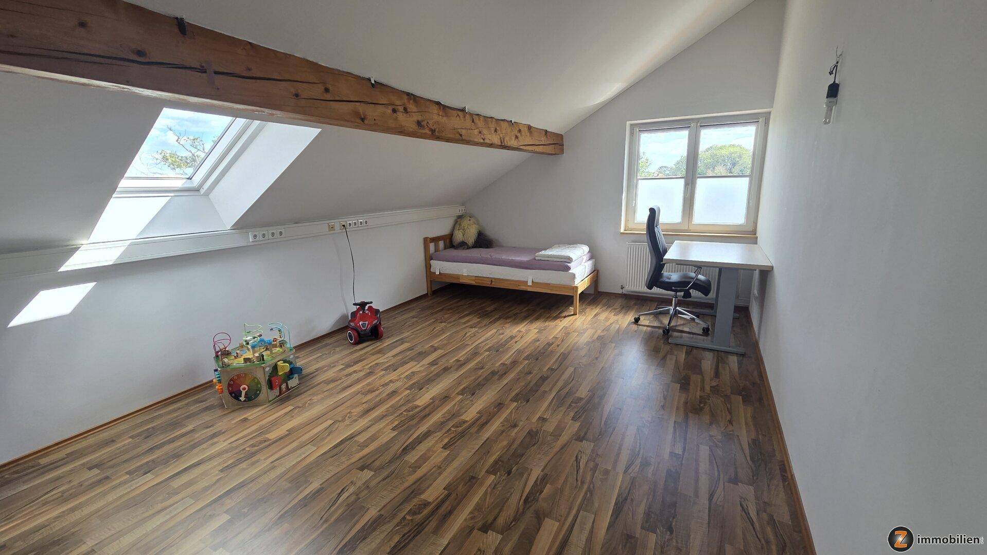 Kinderzimmer im Dachgeschoss mit Laminatboden, Dachfenster und Schreibtisch.