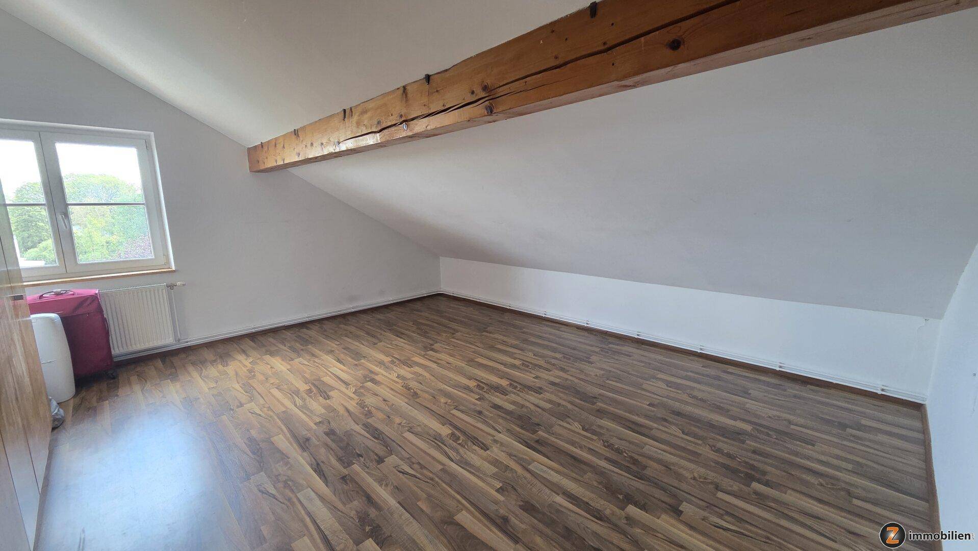 Heller Dachbodenraum mit schrägen Wänden, Holzbalken und Laminatboden.