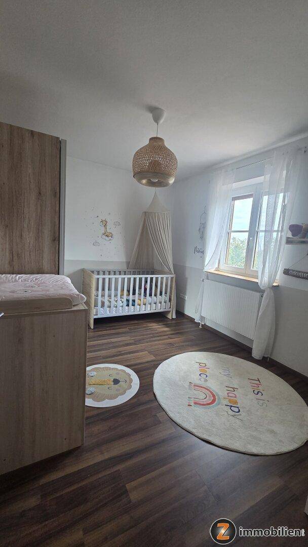 Gemütliches Kinderzimmer mit Holzboden, Babybett und sanfter Beleuchtung.