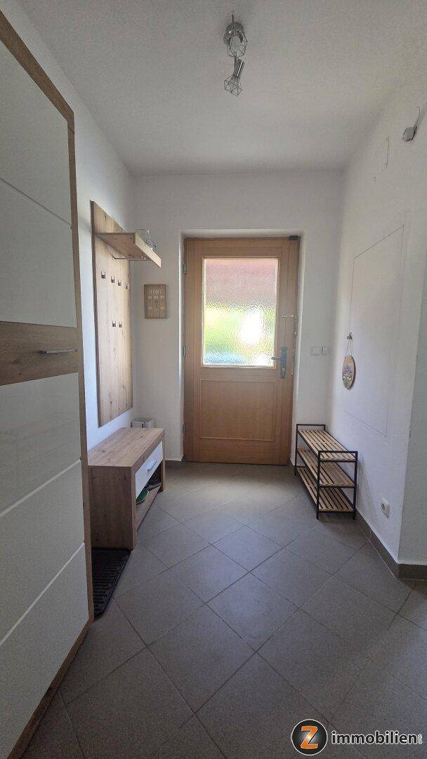 Eingangsbereich mit Fliesenboden, Garderobe und Holztür mit Glaseinsatz.