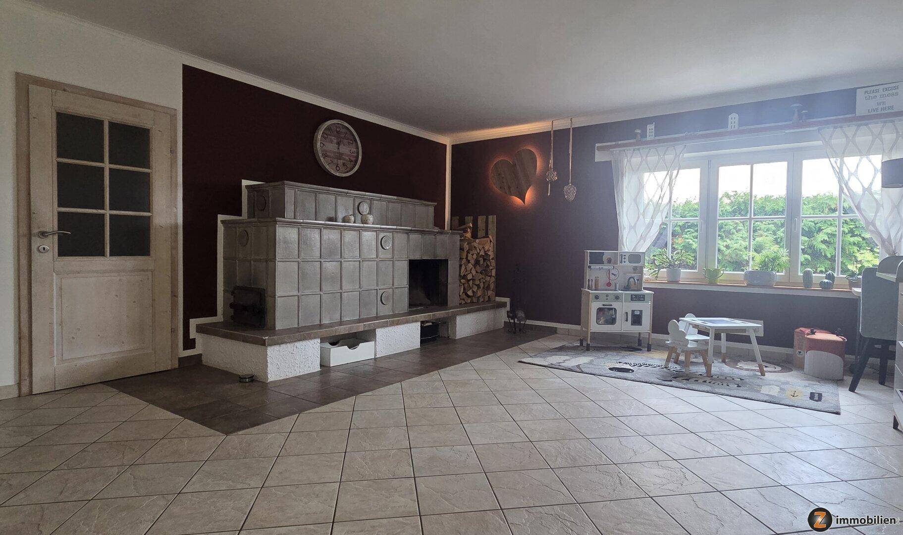 Gemütliches Wohnzimmer mit traditionellem Kachelofen, Fliesenboden und großem Fenster.