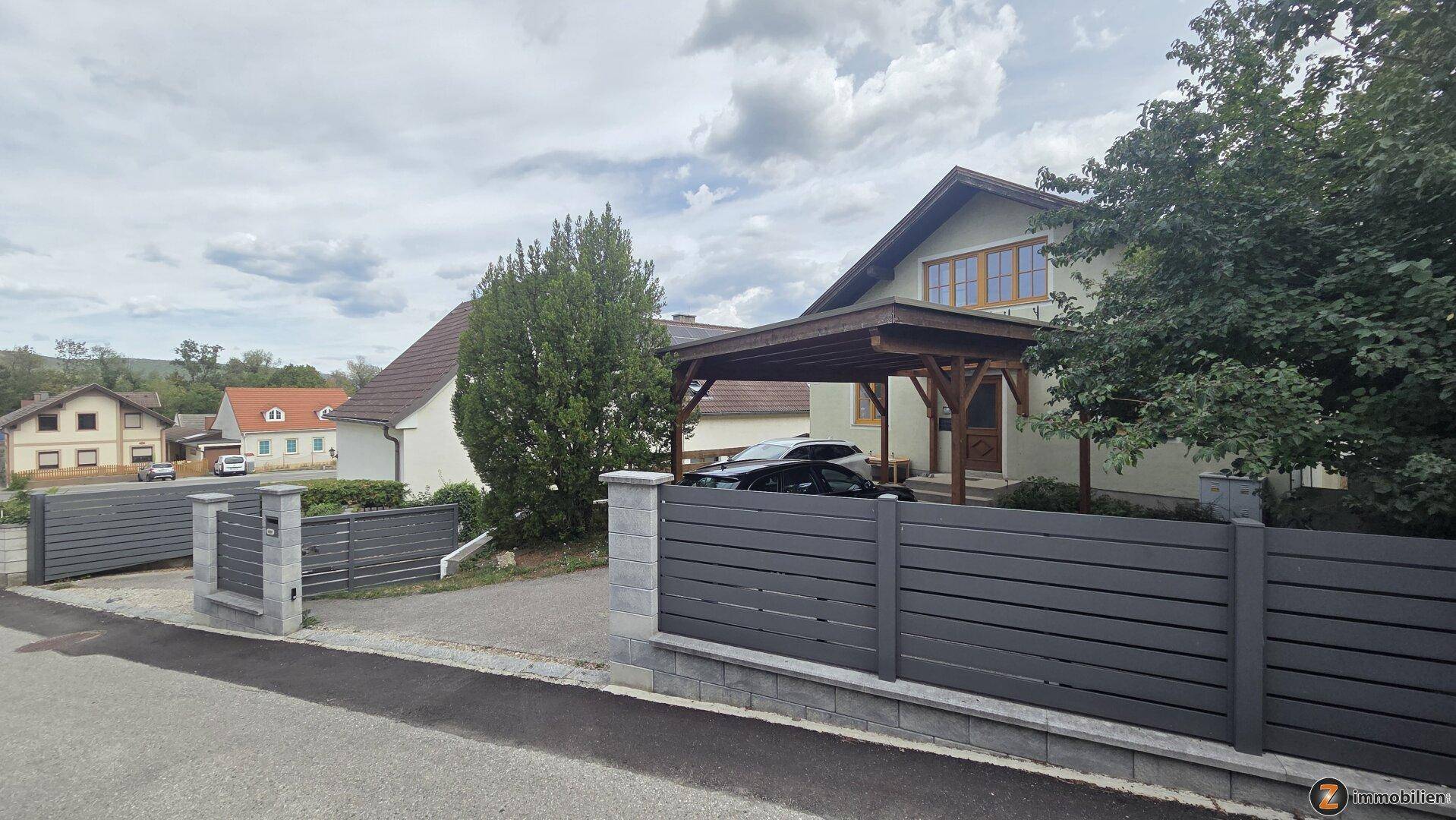 Vorderansicht des Hauses mit modernem Zaun und überdachtem Carport für Fahrzeuge.
