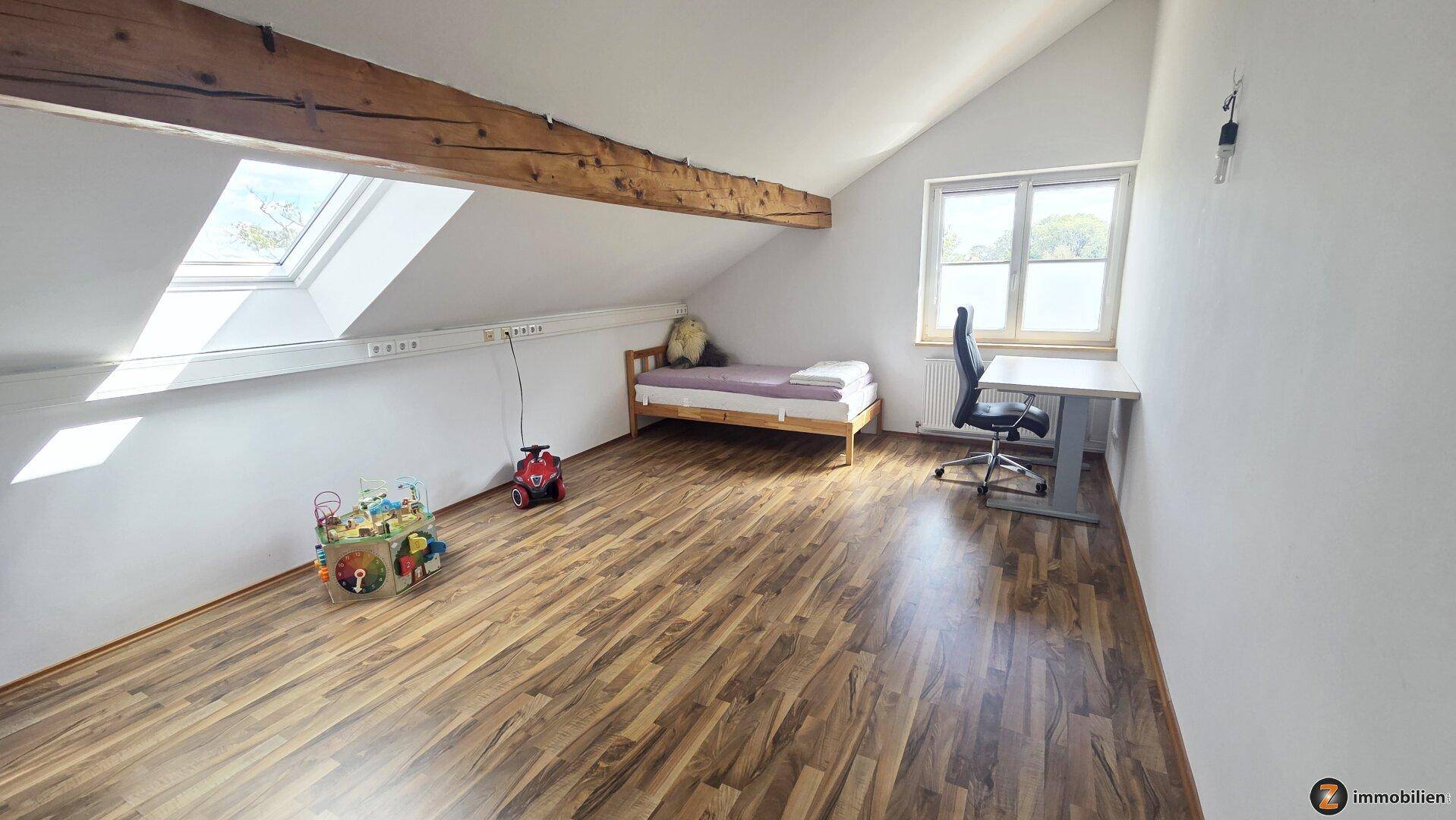 Helles Schlafzimmer im Dachgeschoss mit Holzbalken, Dachfenster und Laminatboden, ideal als Kinderzimmer.