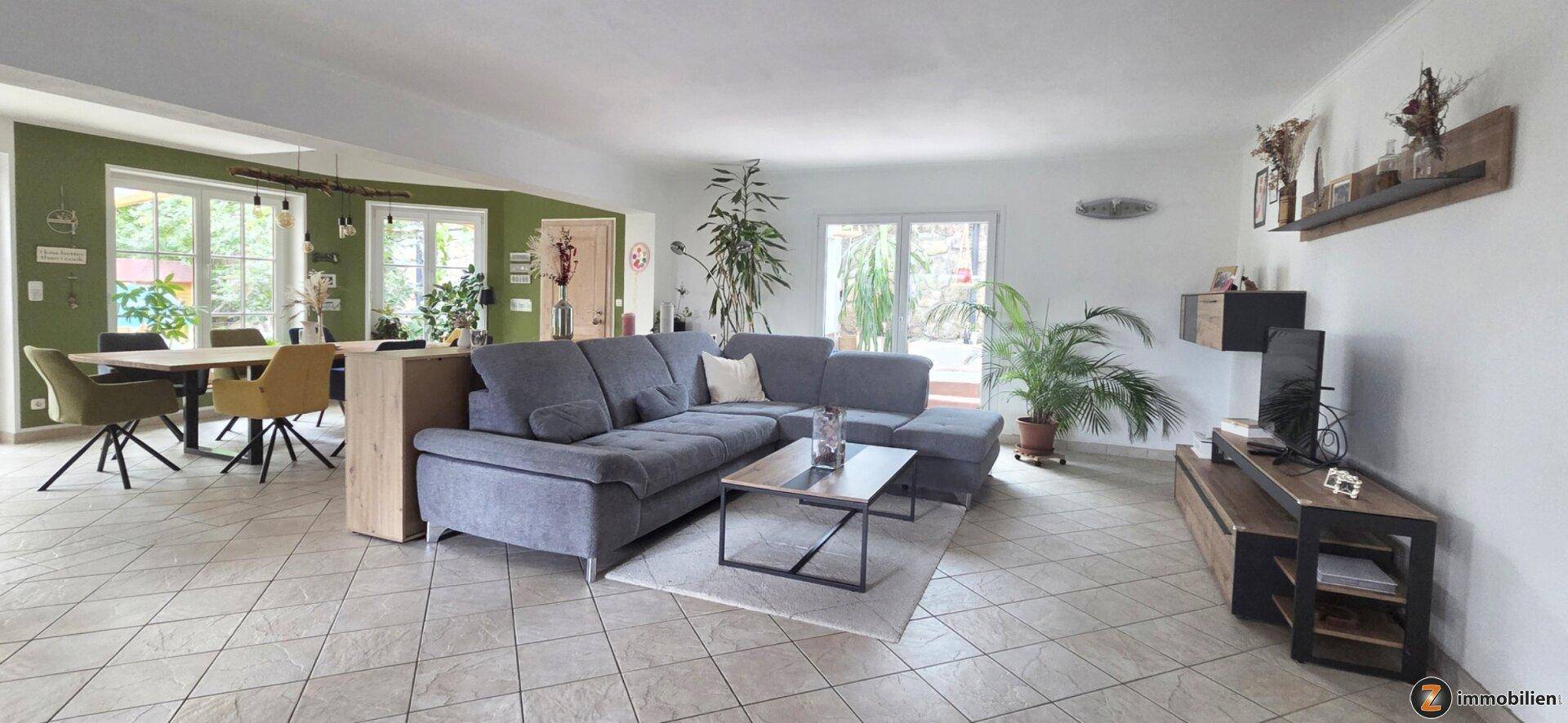 Geräumiger offener Wohn- und Essbereich mit bequemer Couch, großem Esstisch und hellem Fliesenboden.