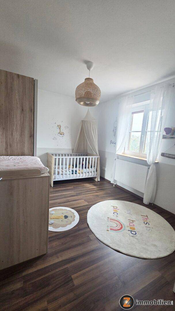 Liebevoll eingerichtetes Kinderzimmer mit Babybett, Wickeltisch und hellem Laminatboden, gut beleuchtet.