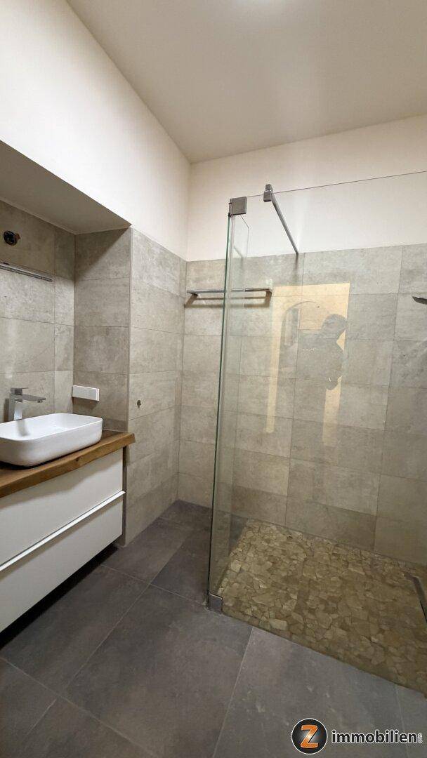 Modernes Badezimmer mit begehbarer Dusche, elegantem Waschbecken und grauen Fliesen.