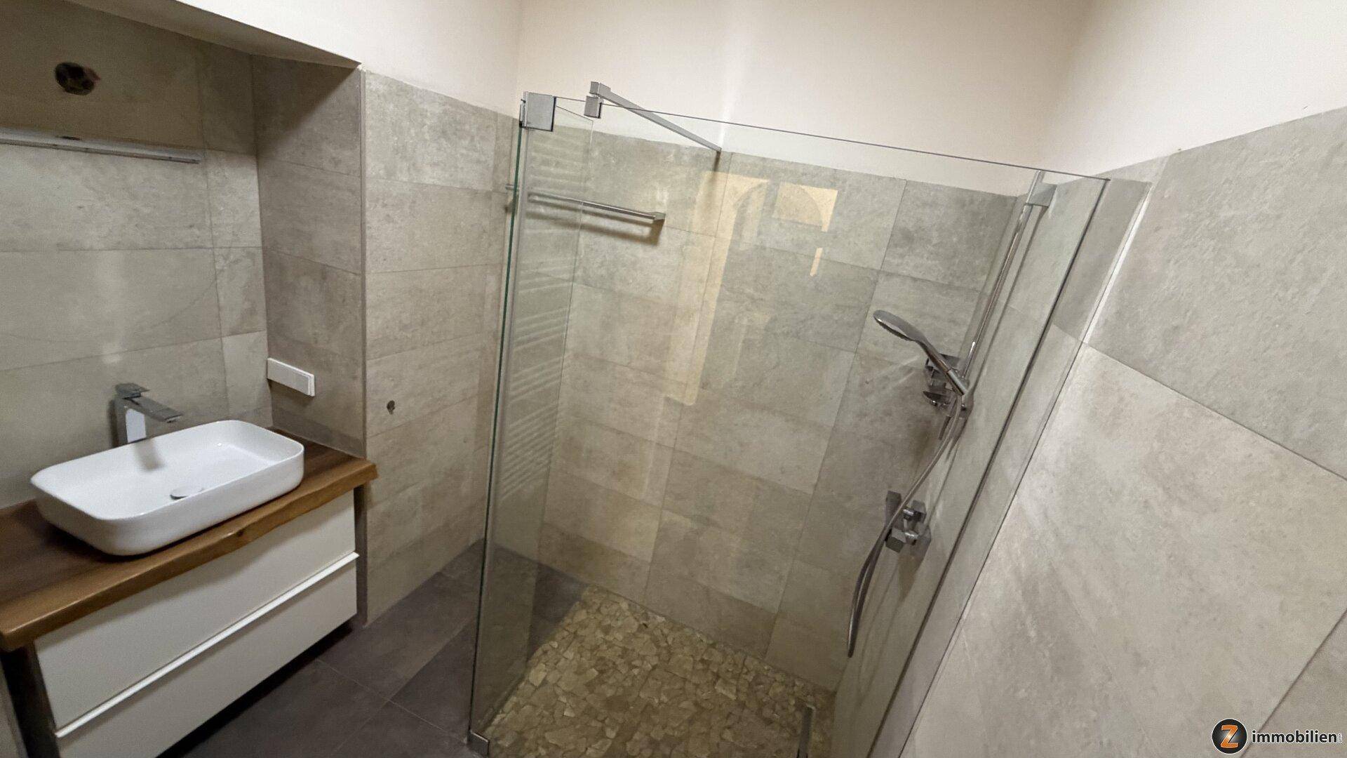 Helles Badezimmer mit geräumiger begehbarer Dusche, modernem Waschtisch und grauen Fliesen.