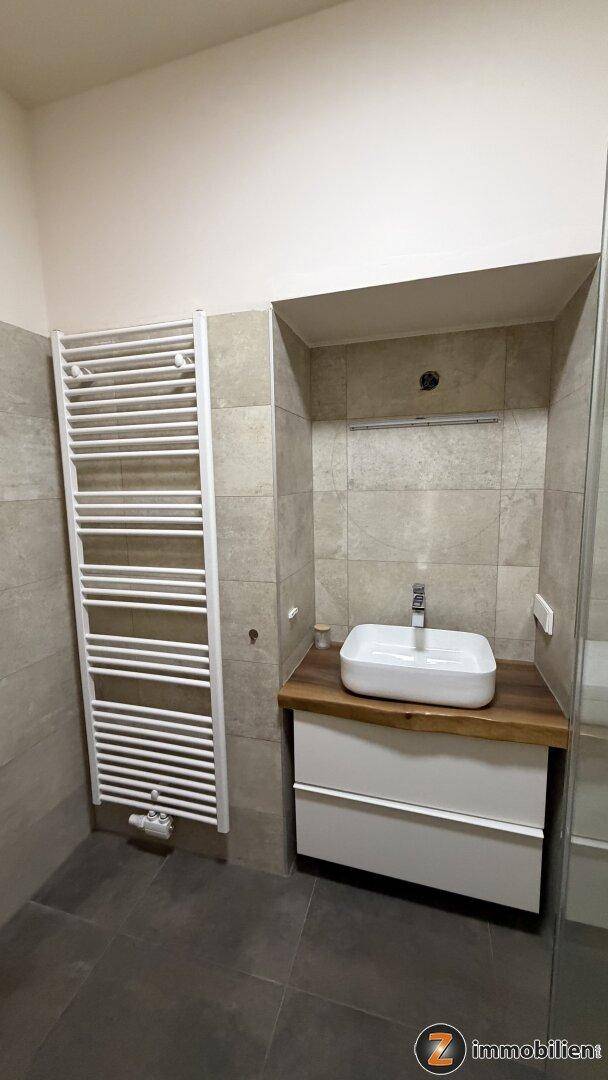 Zeitgemäßes Badezimmer mit beheiztem Handtuchhalter, modernem Waschbecken und grauen Wandfliesen.