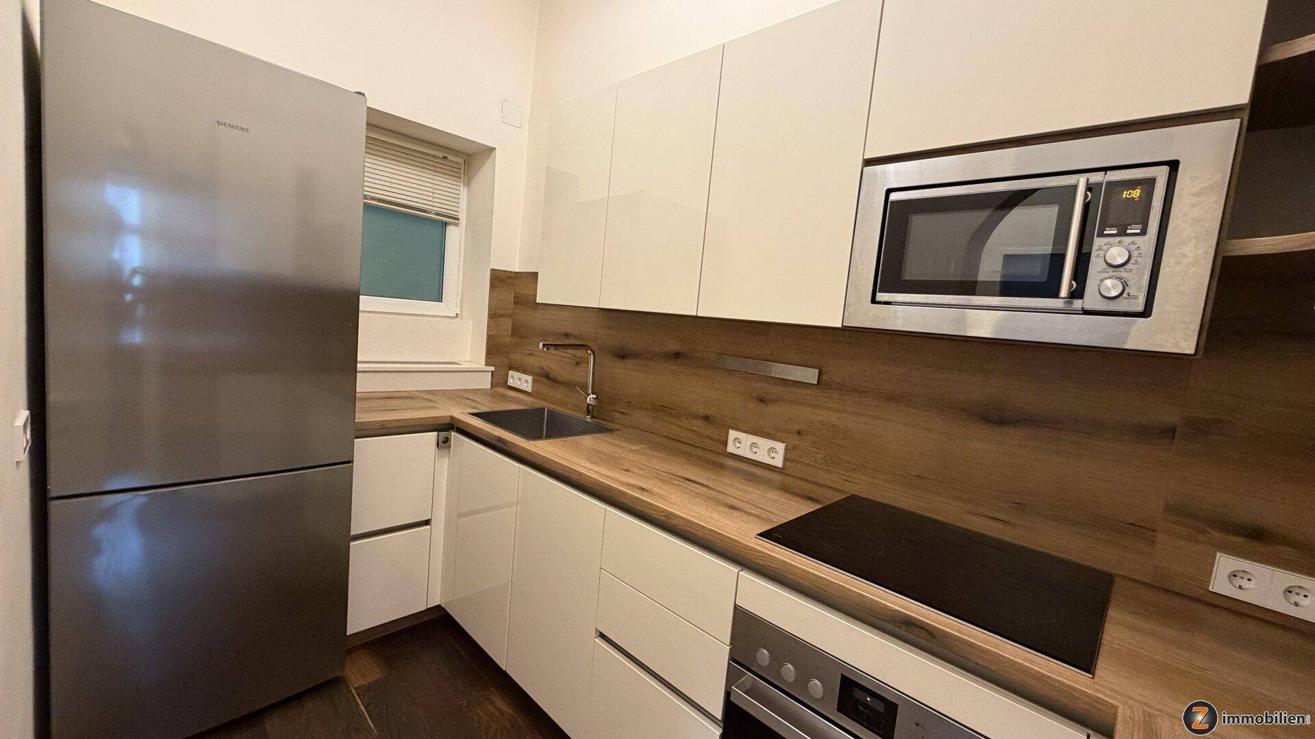 Helle Küche mit modernen Einbaugeräten, Kühlschrank und Fenster für natürliches Licht.