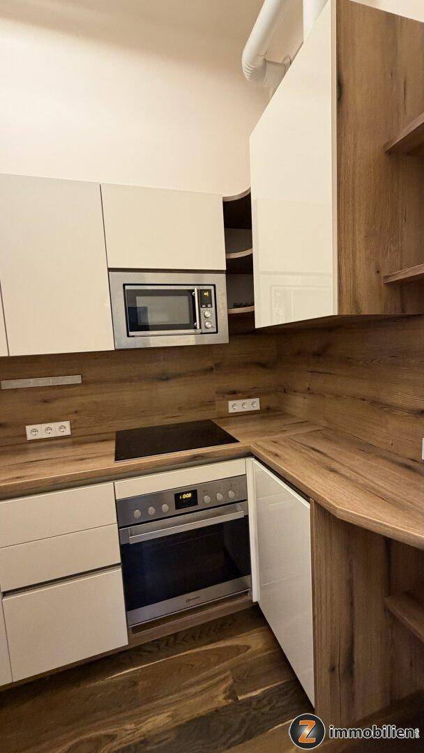 Detailansicht der modernen Küche mit Backofen, Induktionskochfeld und praktischen offenen Regalen.
