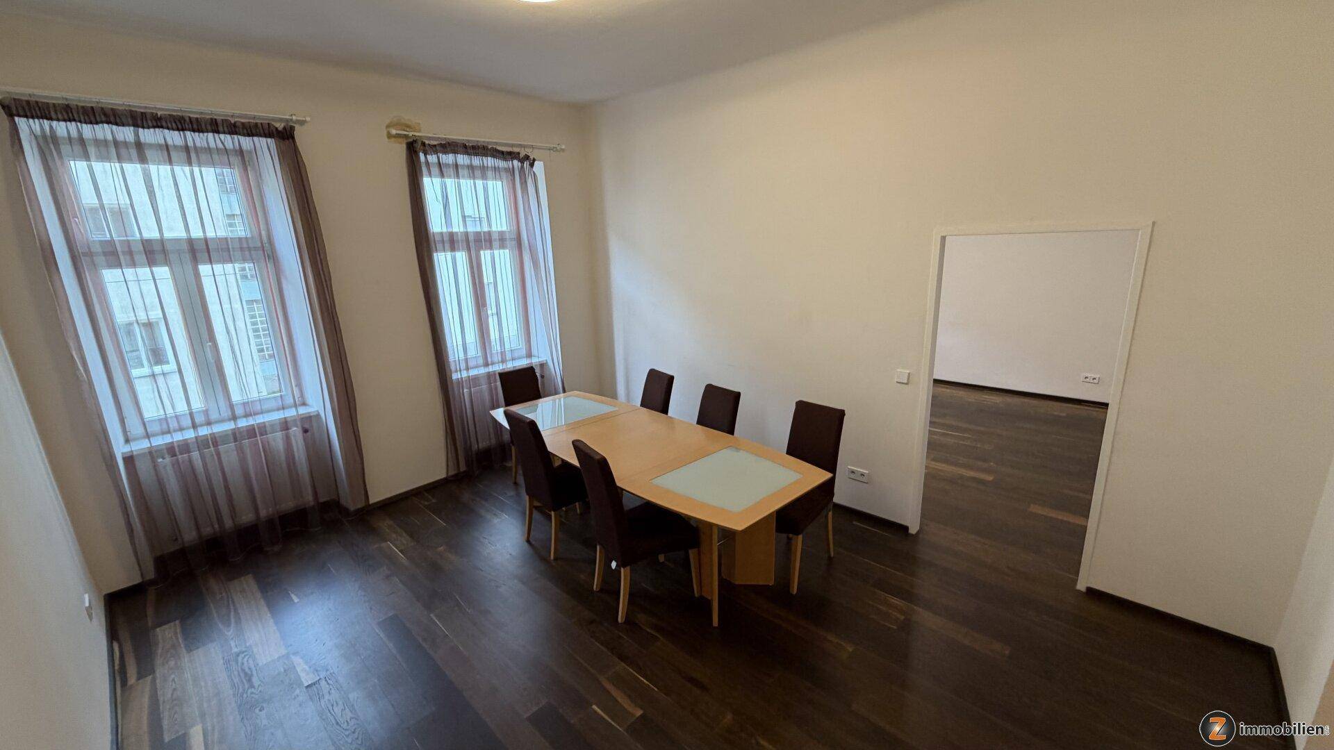 Geräumiges Esszimmer mit dunklem Holzboden, Esstisch und Zugang zu einem weiteren Raum.