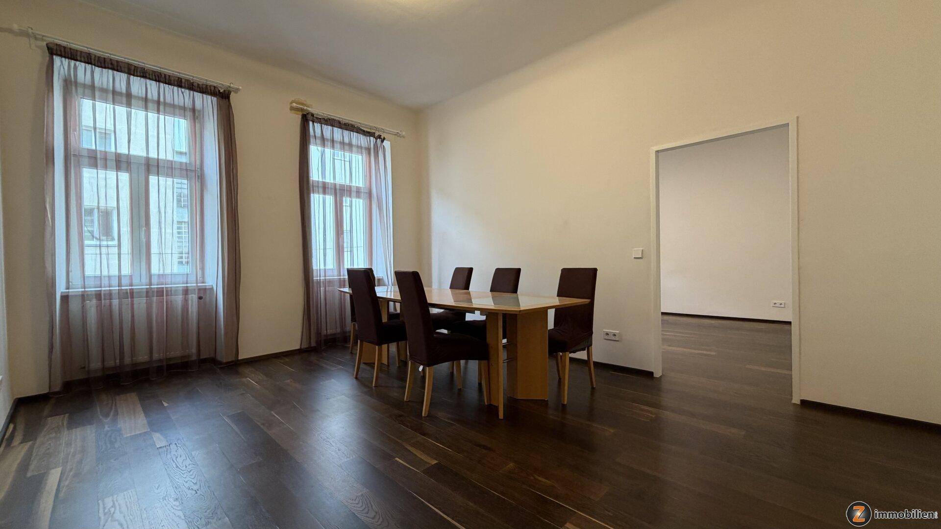 Geräumiges Esszimmer mit dunklem Holzboden, Esstisch und Zugang zu einem weiteren Raum.