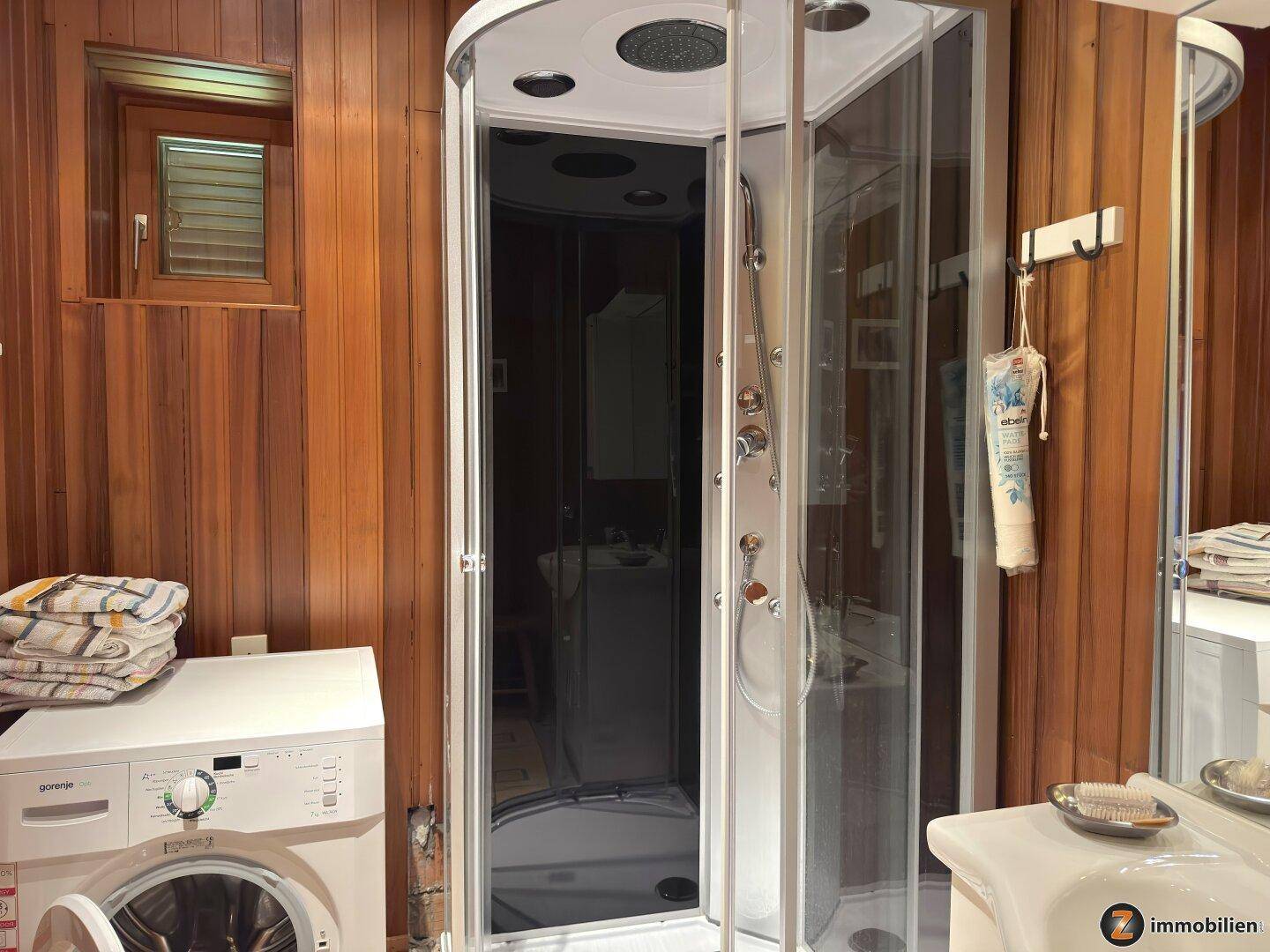 Badezimmer mit Holztäfelung, Duschkabine und Waschmaschine, funktional eingerichtet.