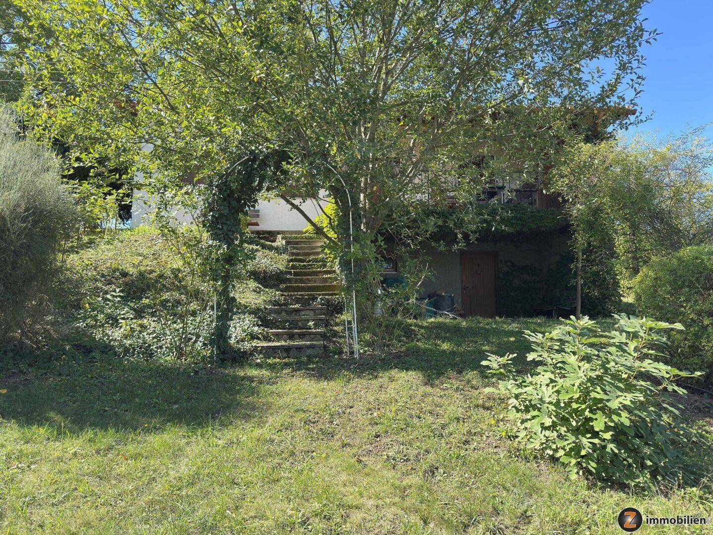 Seitenansicht des Hauses mit Treppe zum Eingang und üppiger Vegetation.