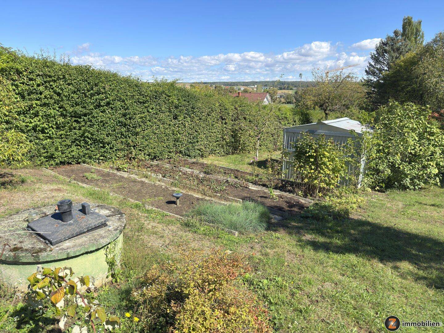 Gartenbereich mit angelegten Beeten, Hecke und Blick in die weite Landschaft.