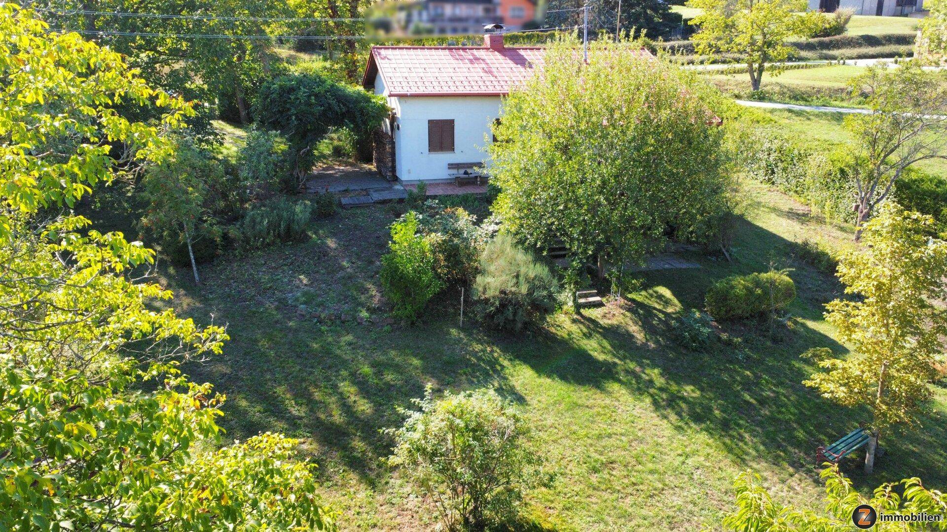 Vogelperspektive des Hauses mit rotem Dach, umgeben von einem großen, grünen Garten.
