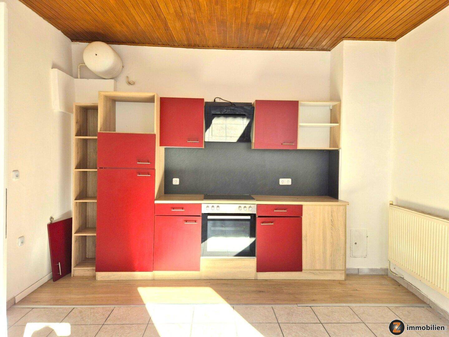 Moderne Einbauküche mit roten Fronten, Holz-Arbeitsplatte und integrierten Geräten unter Holzdecke.