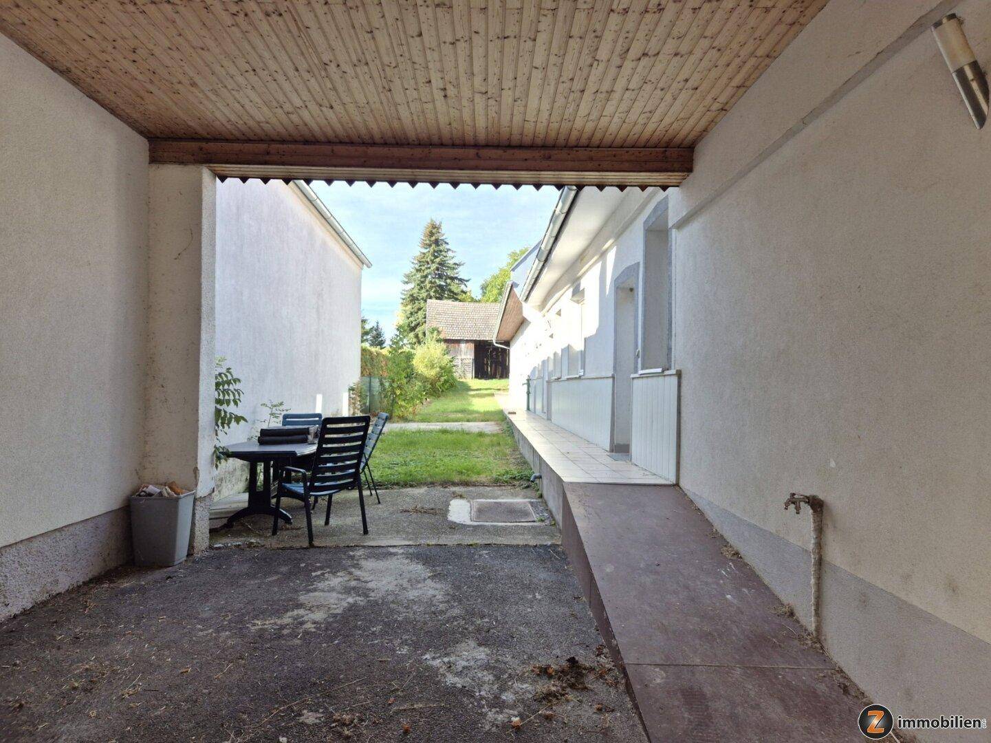 Überdachter Bereich, möglicherweise ein Carport, mit Sitzgelegenheiten und Blick in den Garten.