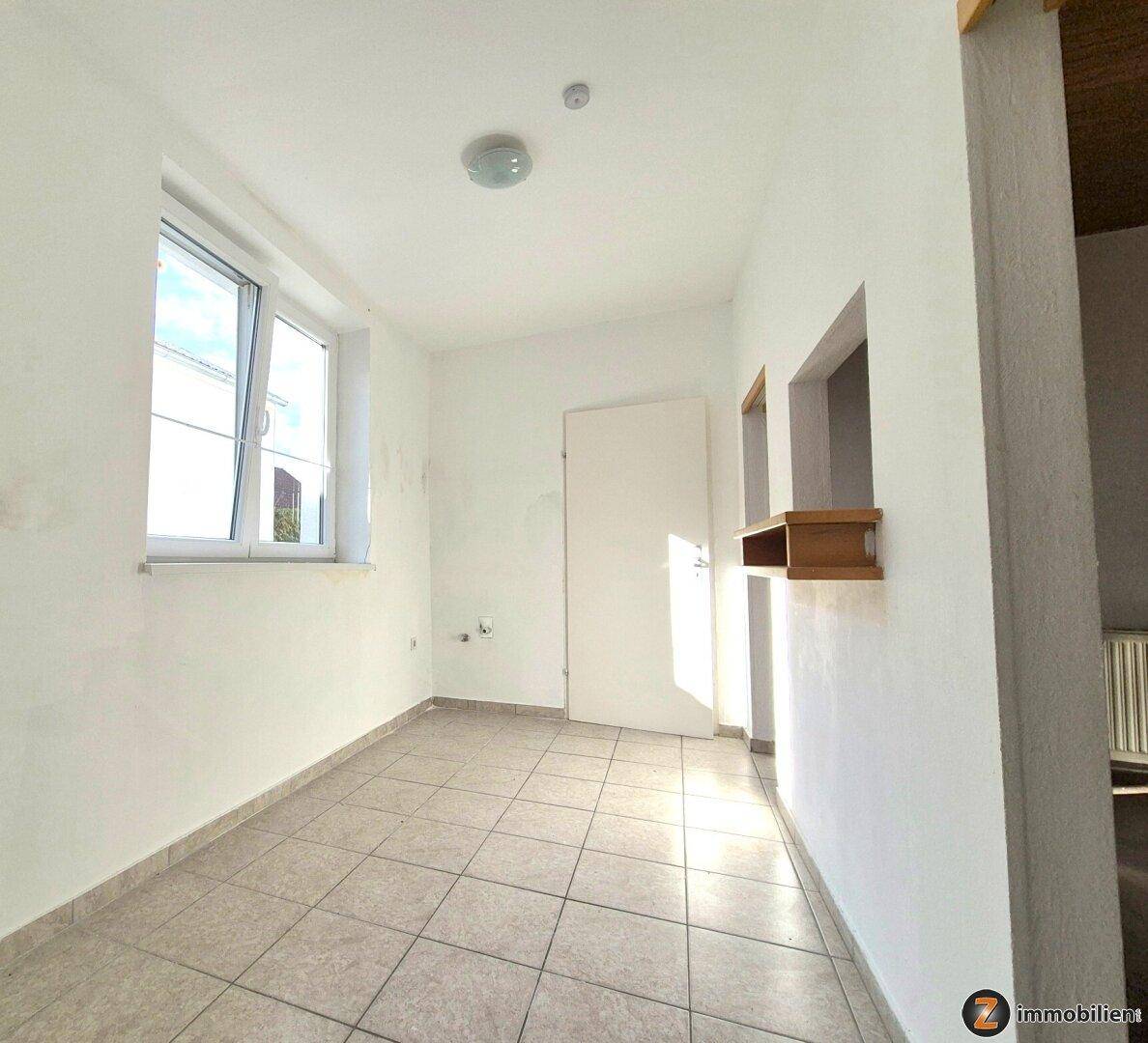 Heller Flur mit Fliesenboden, einem Fenster und einer Tür, die zu weiteren Räumen führt.