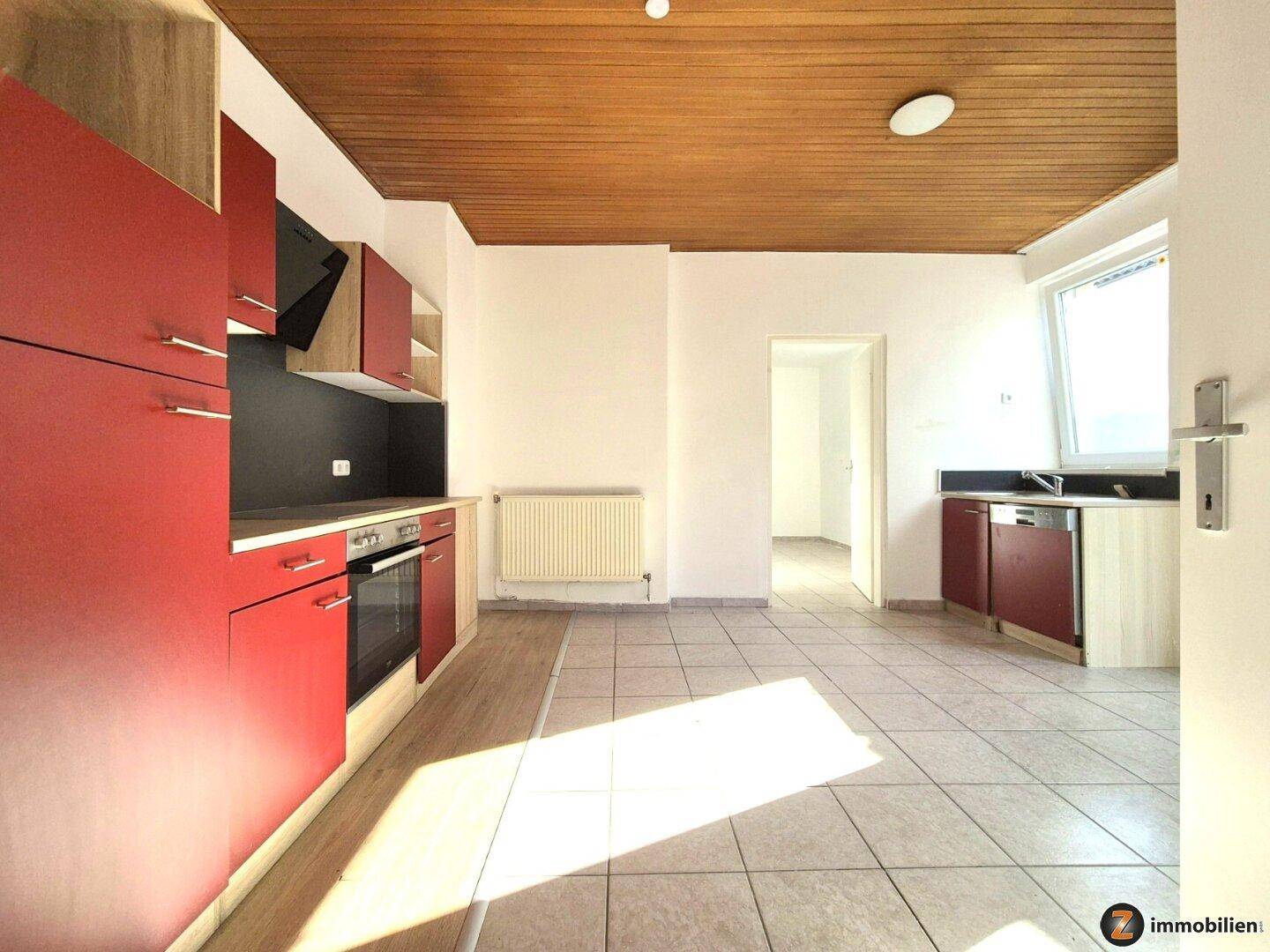 Geräumige Küche mit roten Schränken, Fliesenboden und Holzdeckenverkleidung, bereit zur Nutzung.