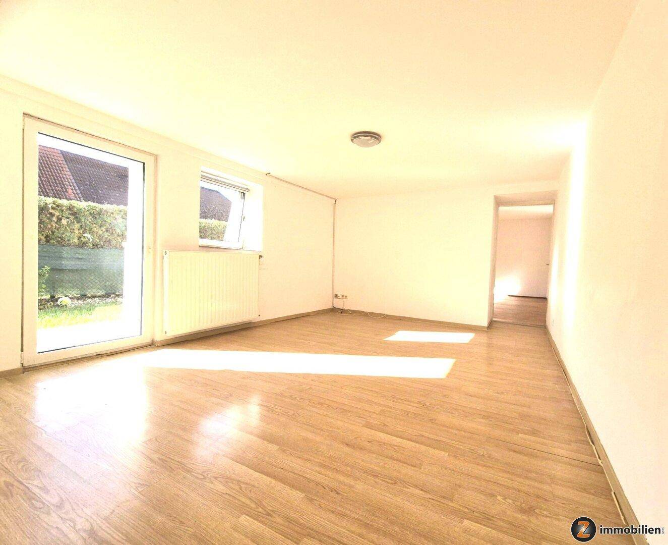 Geräumiges, helles Zimmer mit Laminatboden und Zugang zum Garten durch eine Glastür.