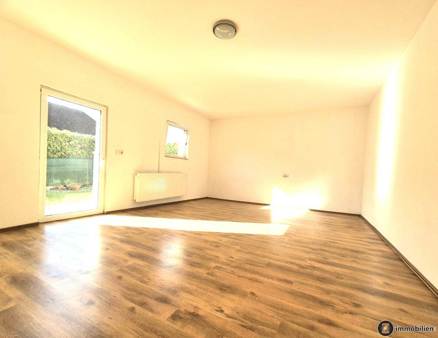 Heller Wohnraum mit Laminatboden und großer Glastür, die viel Tageslicht hereinlässt.