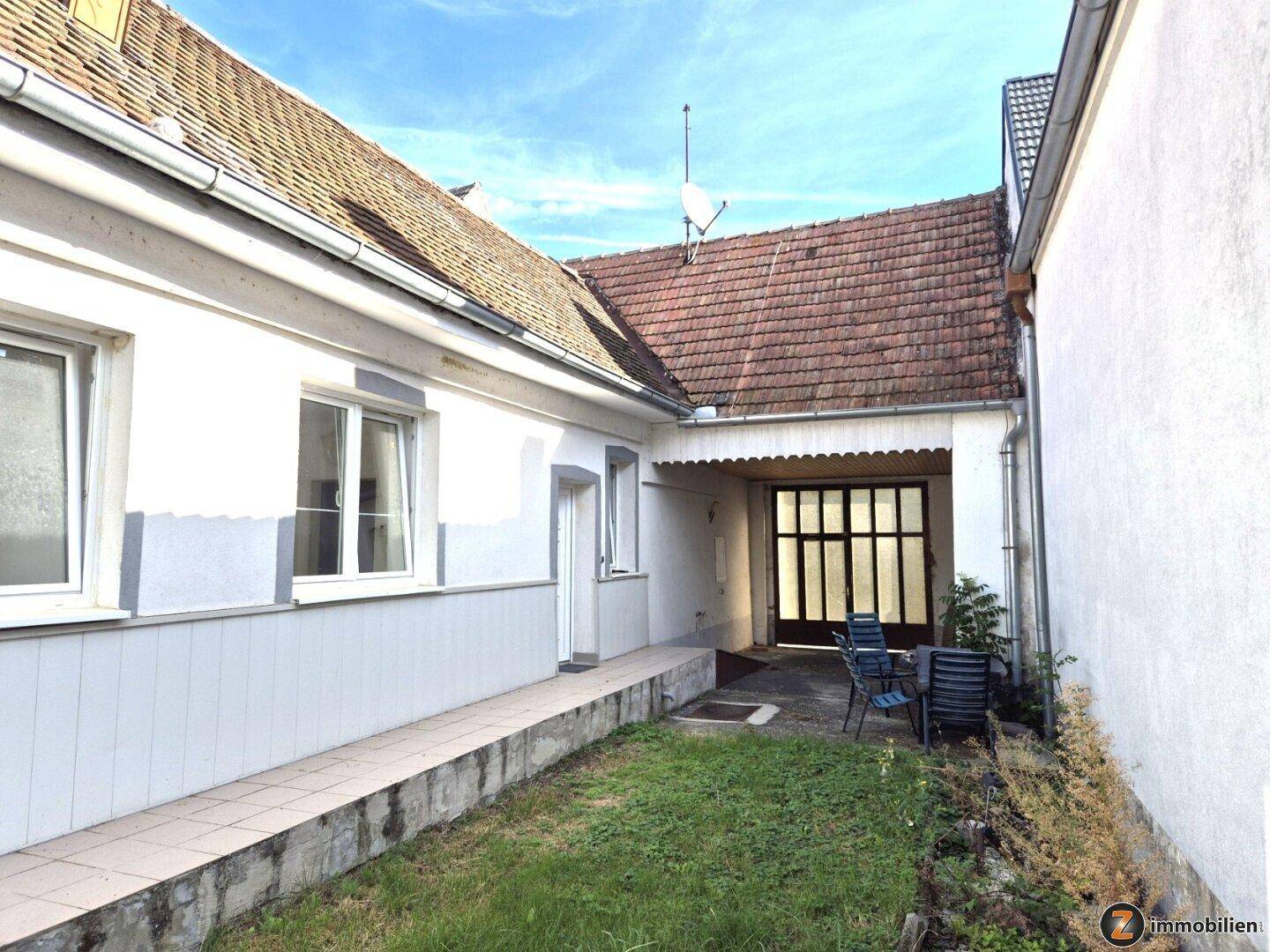 Seitenansicht des Hauses mit überdachtem Bereich, Rasenfläche und Blick auf das Ziegeldach.