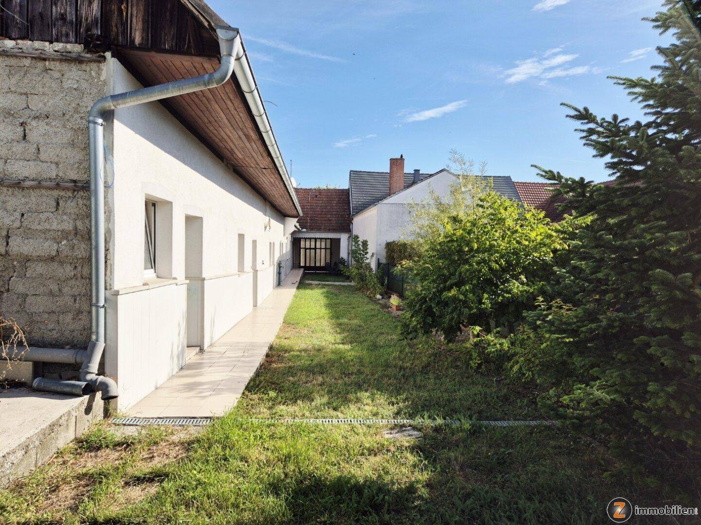Langer Gartenbereich entlang der Hausfassade mit grünem Rasen und einem gepflasterten Weg.