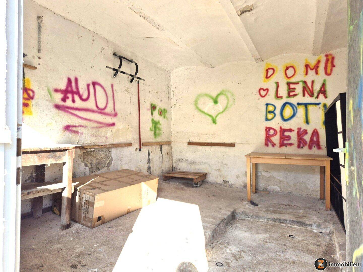 Rustikaler Abstellraum mit Betonboden und bunten Graffiti an den Wänden, bietet viel Stauraum.