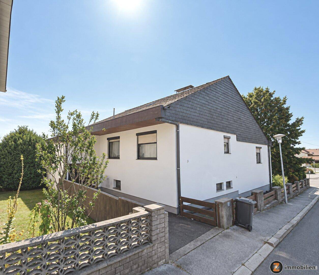 Seitenansicht eines Einfamilienhauses mit weißer Fassade, Schieferdach und gepflegtem Vorgarten.