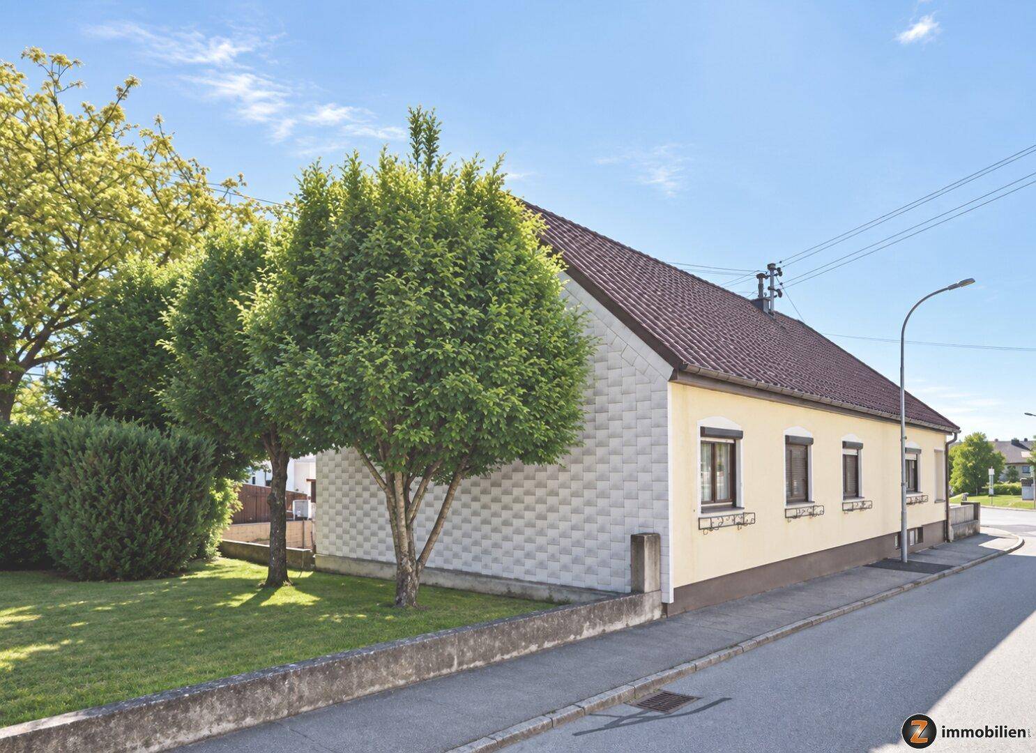 Seitenansicht des Einfamilienhauses mit gepflegtem Rasen und Bäumen im Vorgarten.