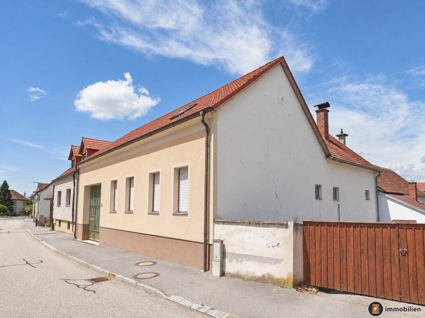 Seitenansicht des Wohnhauses mit Giebeldach, Schornstein und Holzzaun an der Grundstücksgrenze.