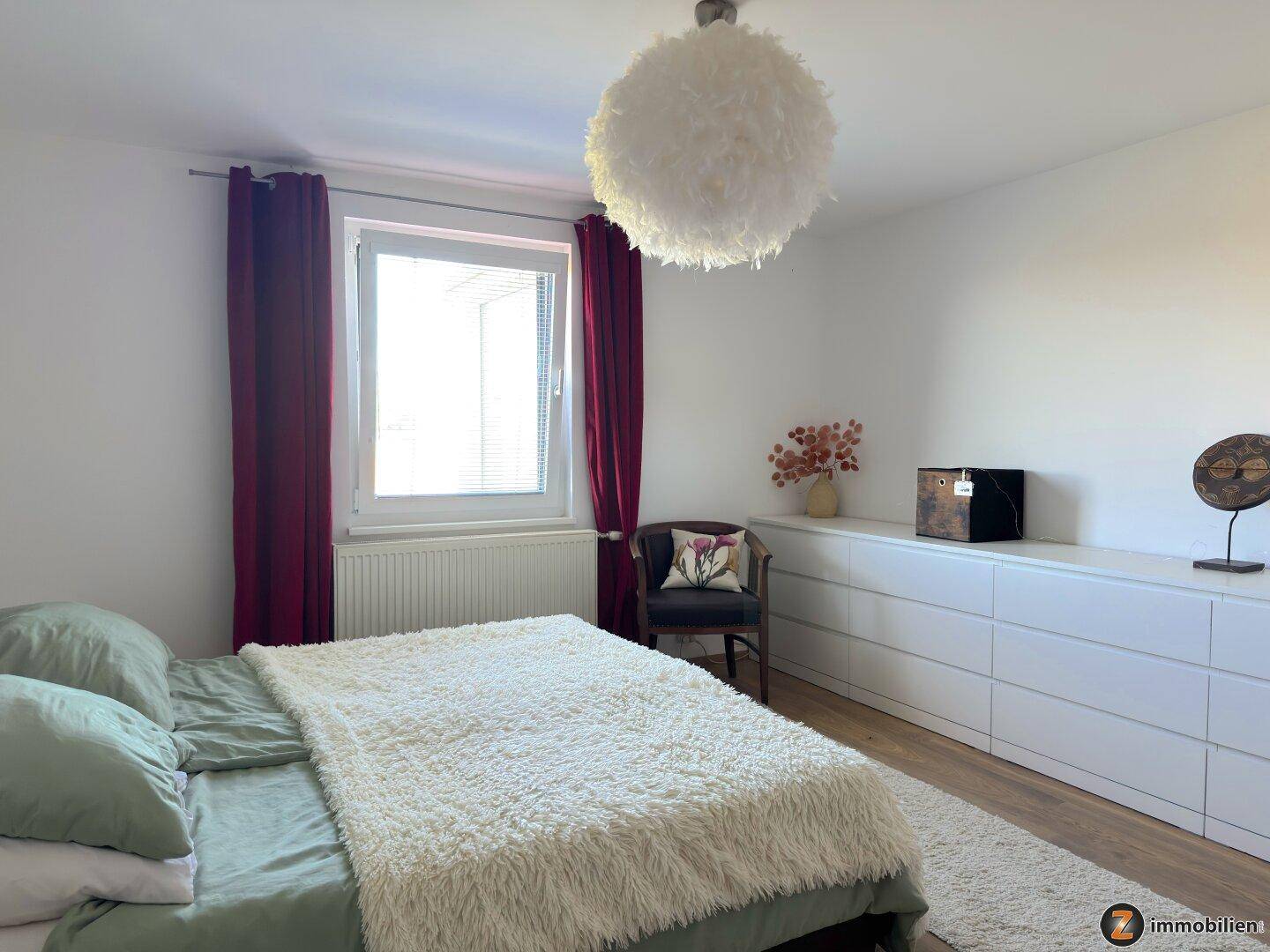 Schlafzimmer mit Doppelbett, Fenster und langen weißen Kommoden entlang der Wand.