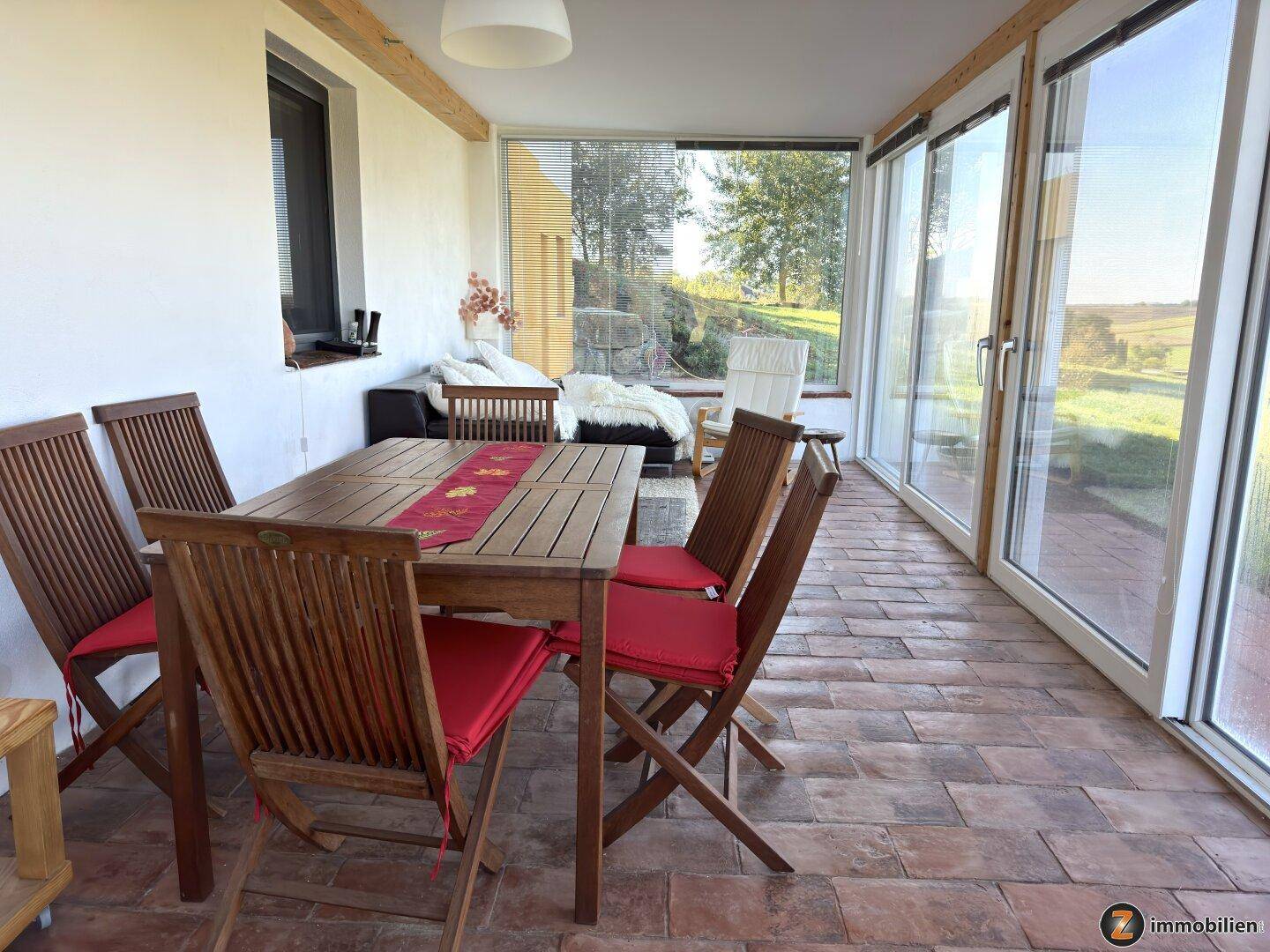 Heller Wintergarten mit Esstisch, Terracotta-Boden und weitem Blick ins Grüne.