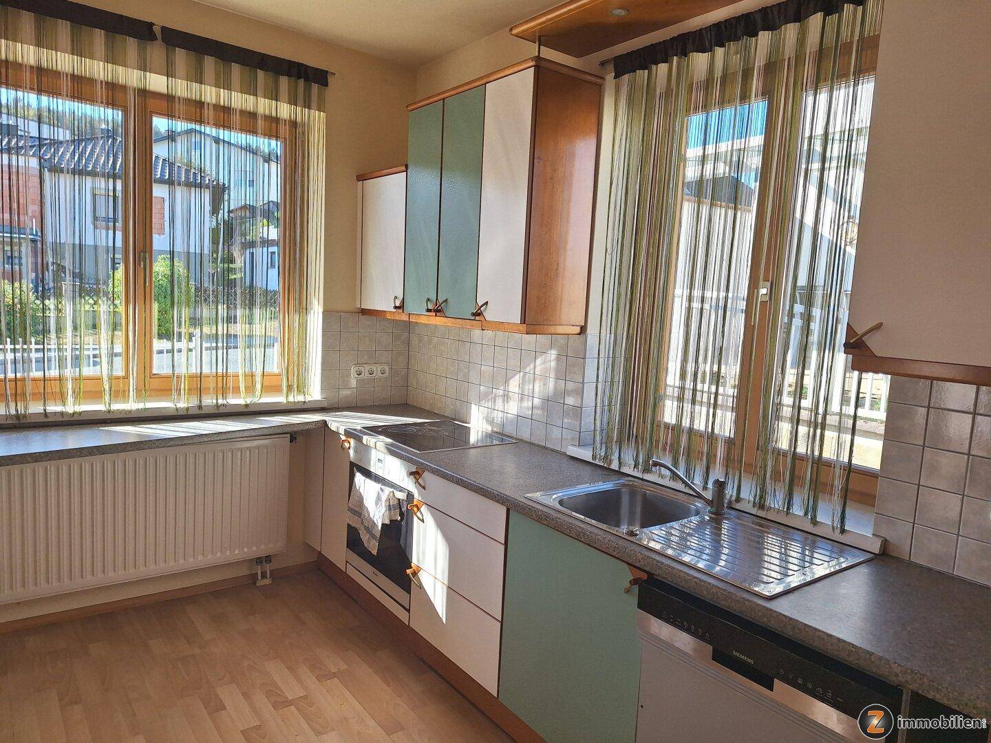 Helle Küche mit Spüle, Kochfeld und Blick auf die Straße durch große Fenster.