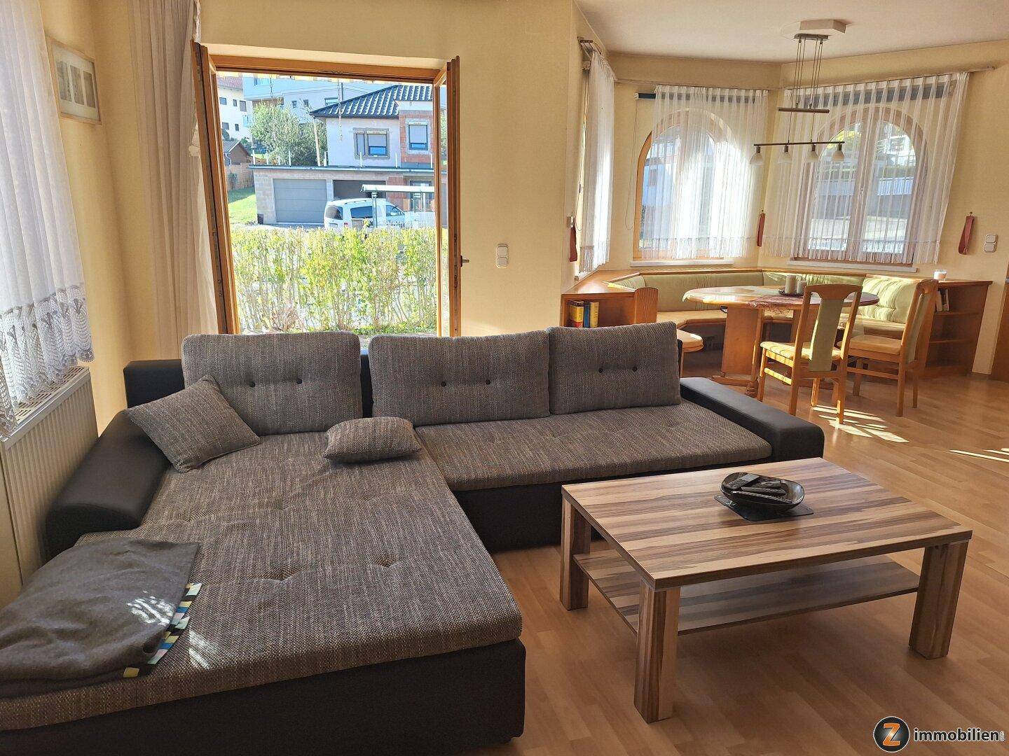 Helles Wohnzimmer mit Ecksofa und Zugang zu einem Außenbereich.