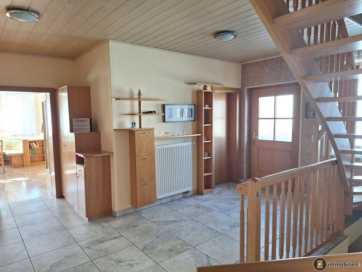 Heller Eingangsbereich mit Holztreppe und Fliesenboden, bietet Zugang zu den oberen Etagen.