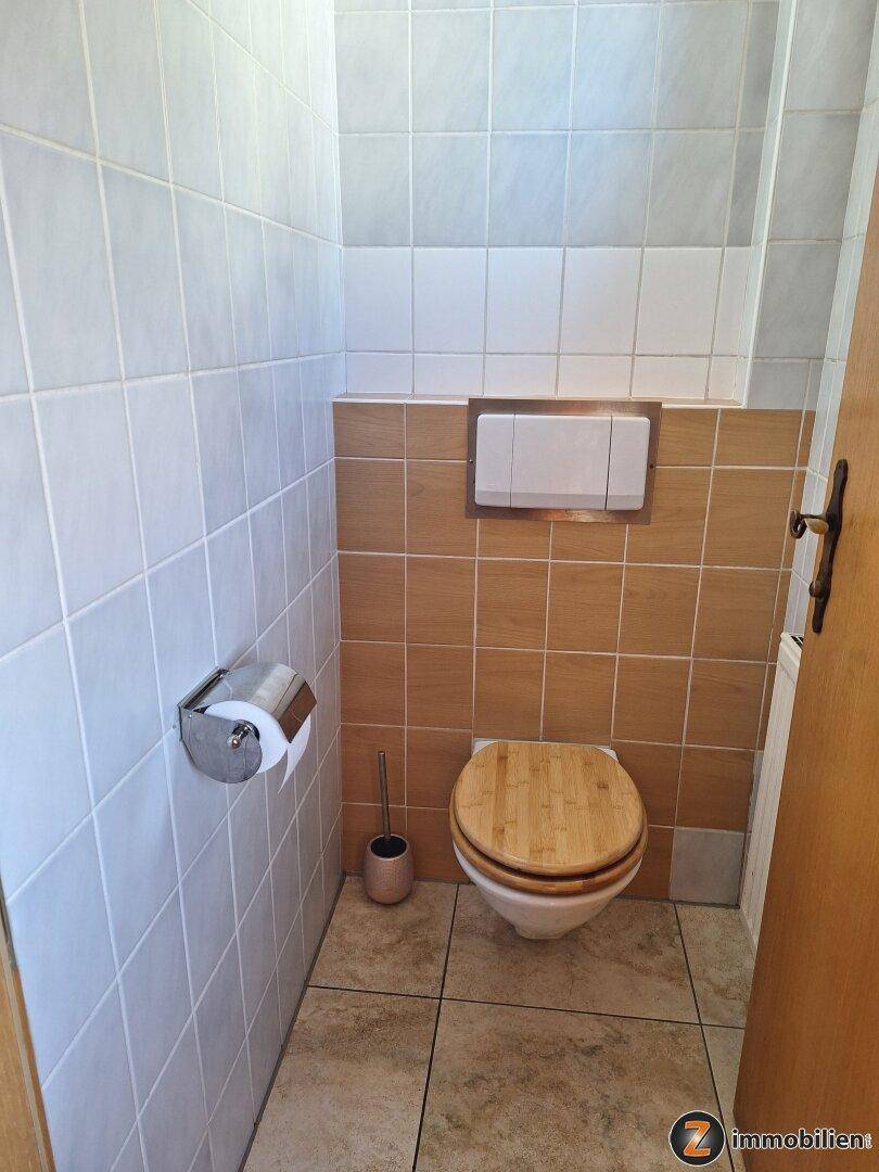 Separate Toilette mit Fliesen an Wänden und Boden, ausgestattet mit Holz-WC-Sitz.