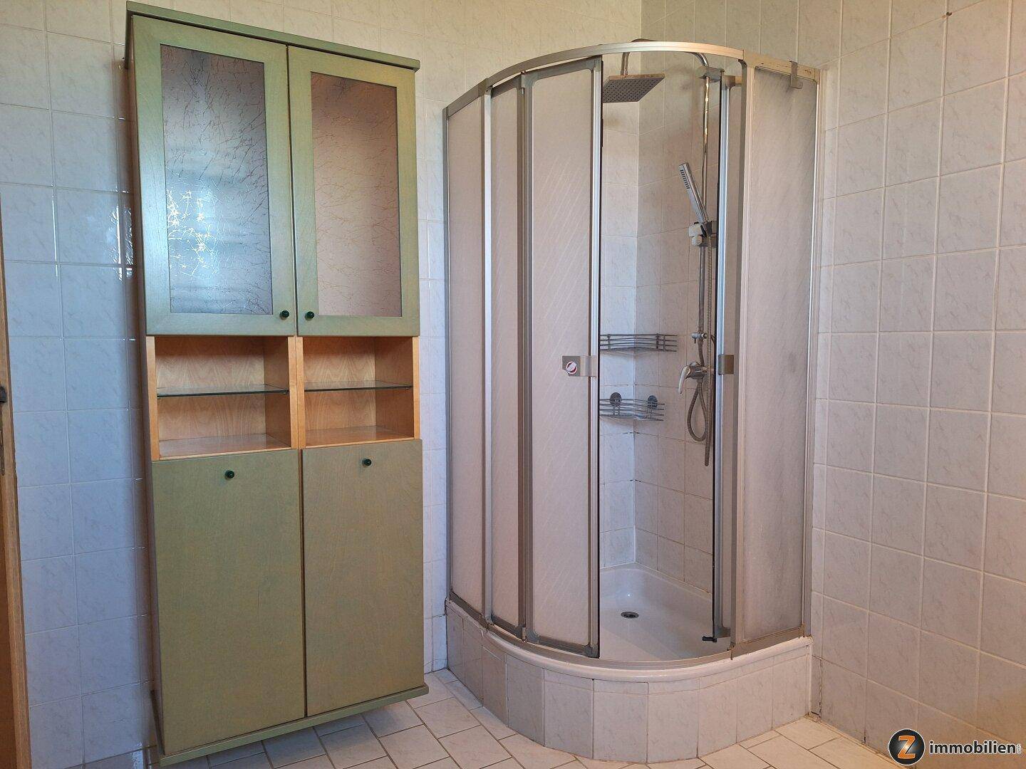 Badezimmer mit Duschkabine und Stauraumschrank, gefliesten Wänden und Boden.