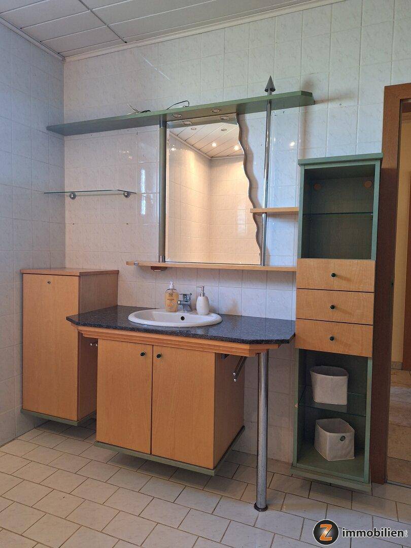 Badezimmer mit Einzelwaschbecken und Spiegelschrank, umgeben von Fliesen.