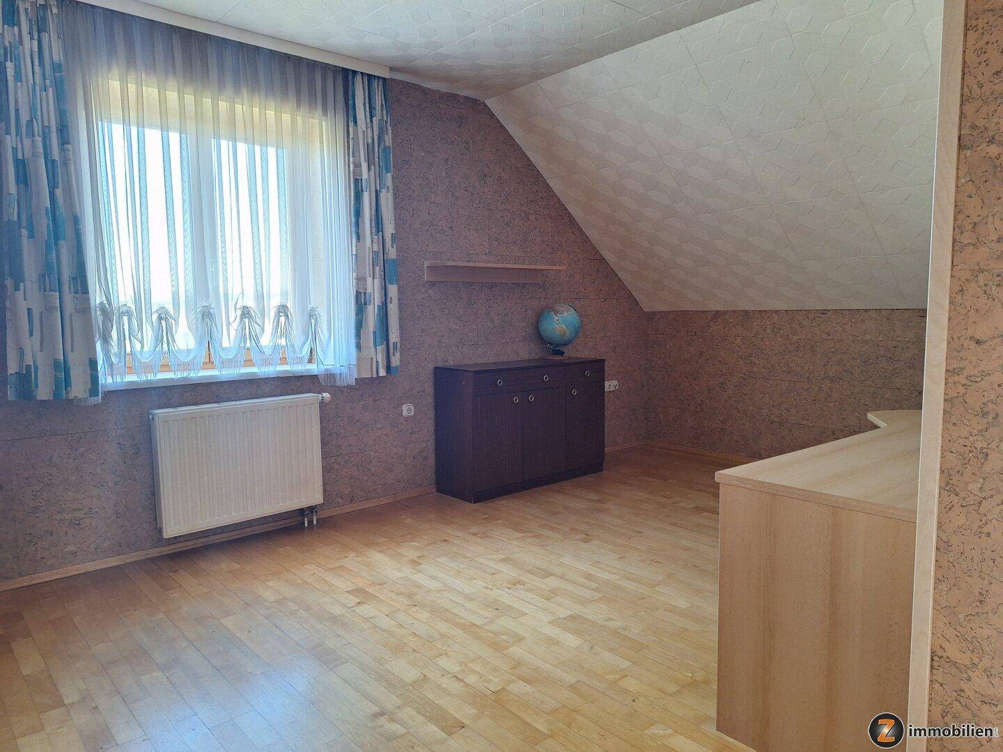 Geräumiges Schlafzimmer im Dachgeschoss mit Holzboden und großem Fenster.