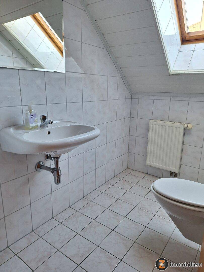 Dachgeschoss-Badezimmer mit Waschbecken und Toilette, hell gefliest.