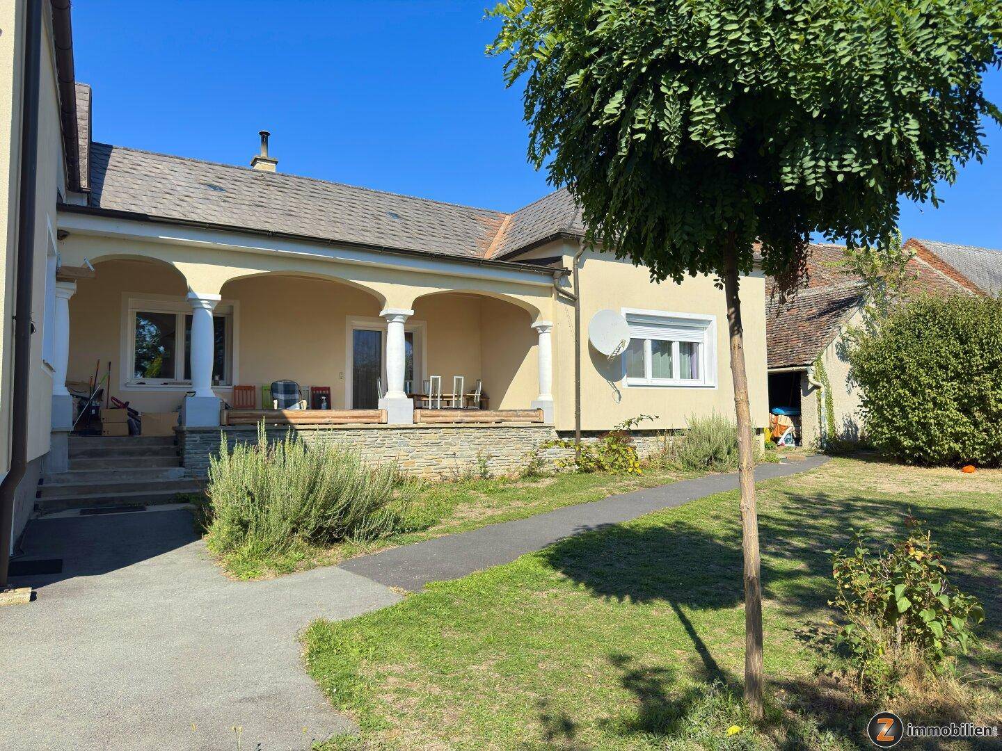 Charmante Hausfassade mit überdachter Terrasse und Gartenweg.