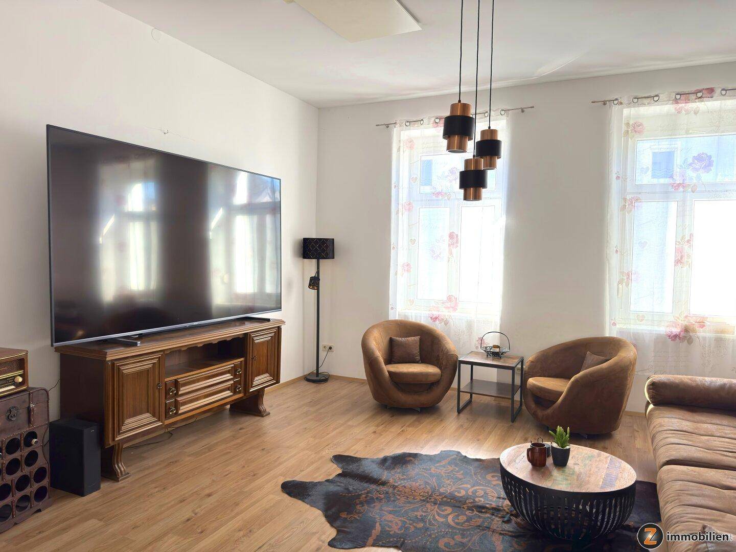 Gemütliches Wohnzimmer mit großem Fernseher, bequemen Sesseln und Holzboden.